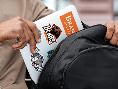 Student taking a laptop covered in school stickers out of a backpack